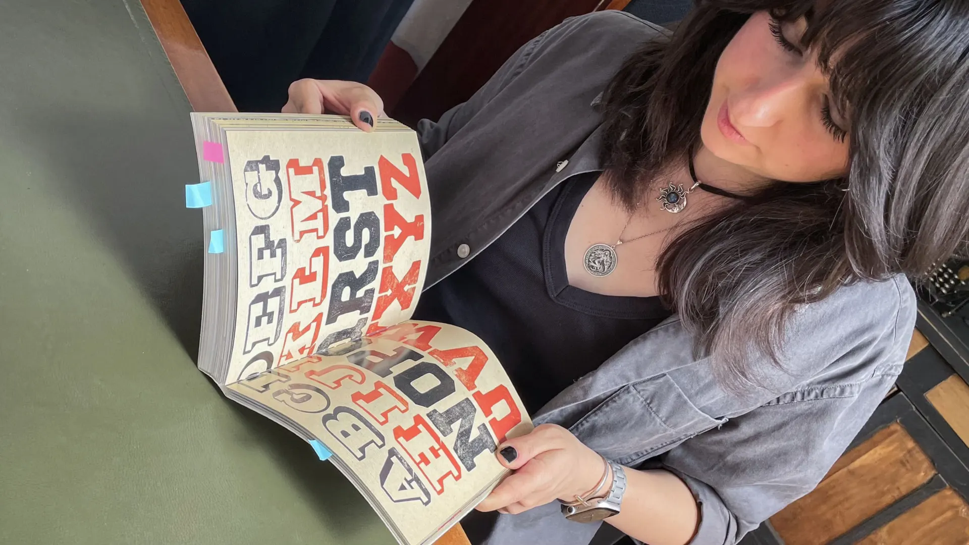 Laurie leafing through a wood type specimen book with large red and black letterpress letters
