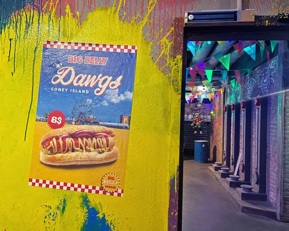 Big Belly Dawgs Coney Island poster on a paint-splashed wall beside an immersive alley