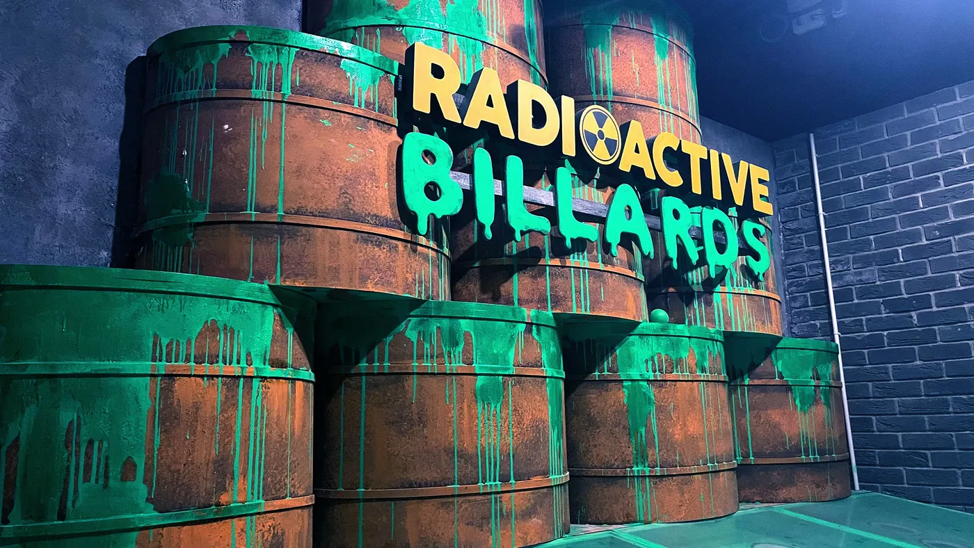 Radioactive Billiards signage on green toxic barrels in the immersive set