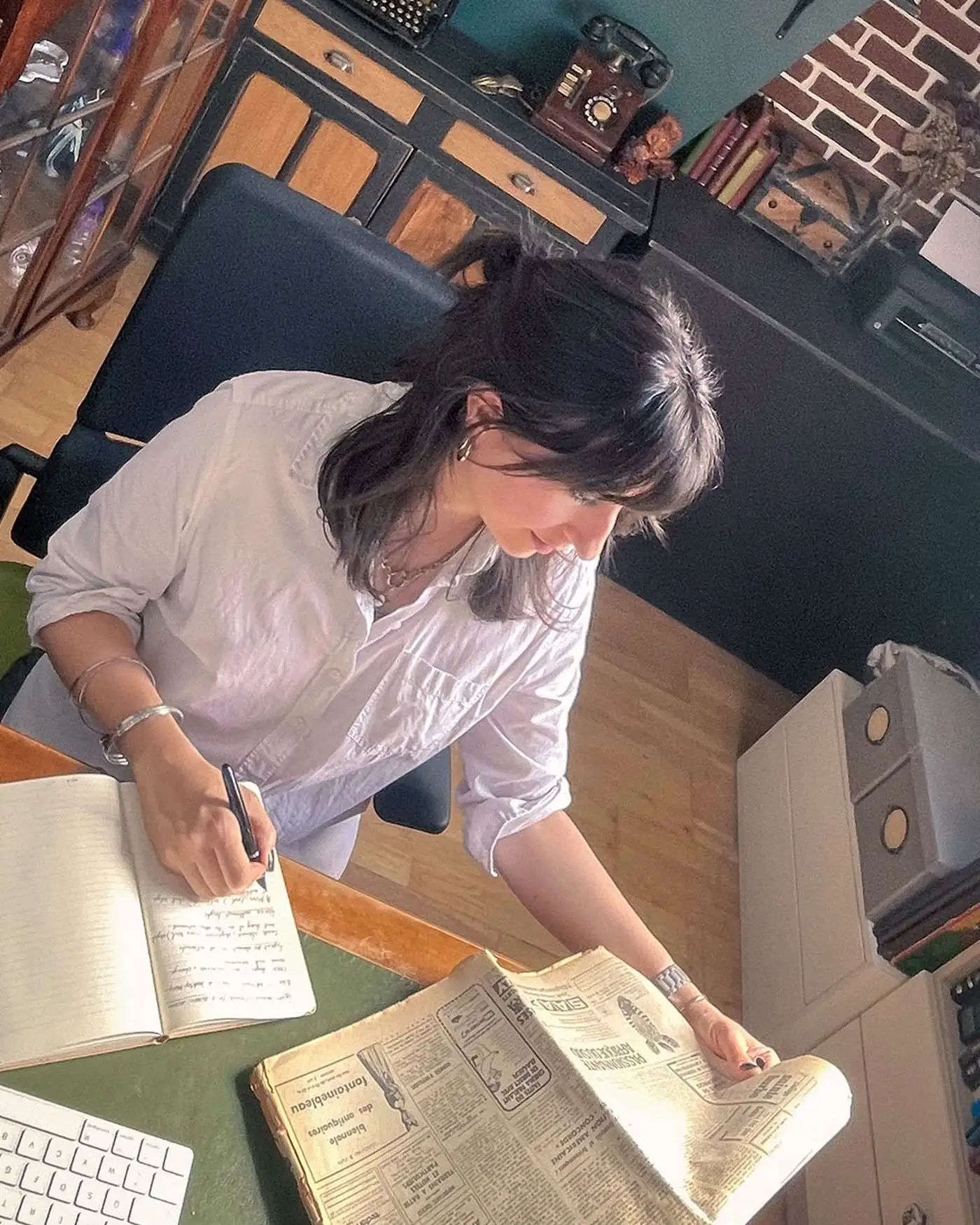 The designer taking notes at her desk beside a vintage newspaper during historical research