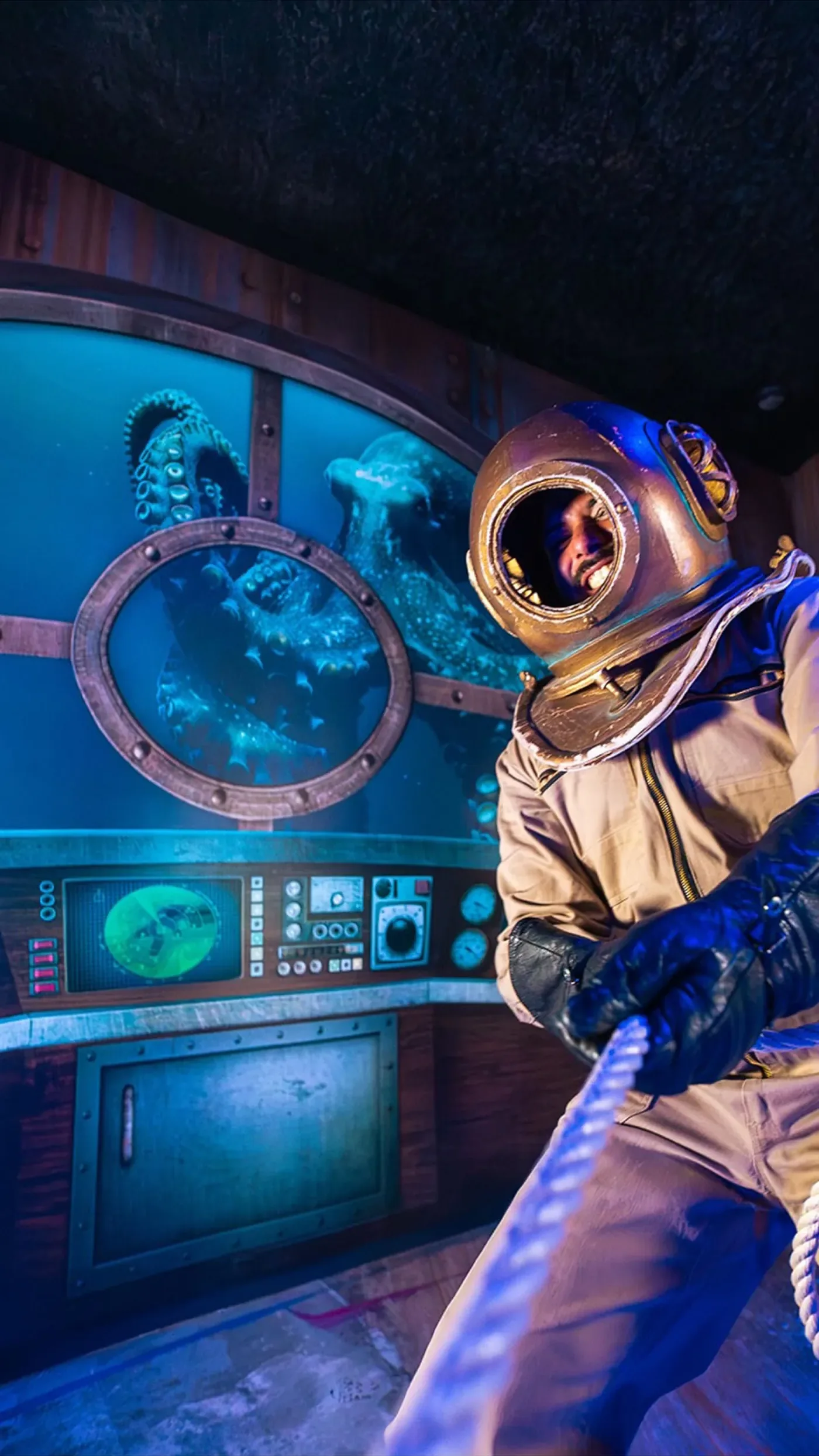 A diver in a vintage brass-helmet suit at the controls of the immersive submarine set