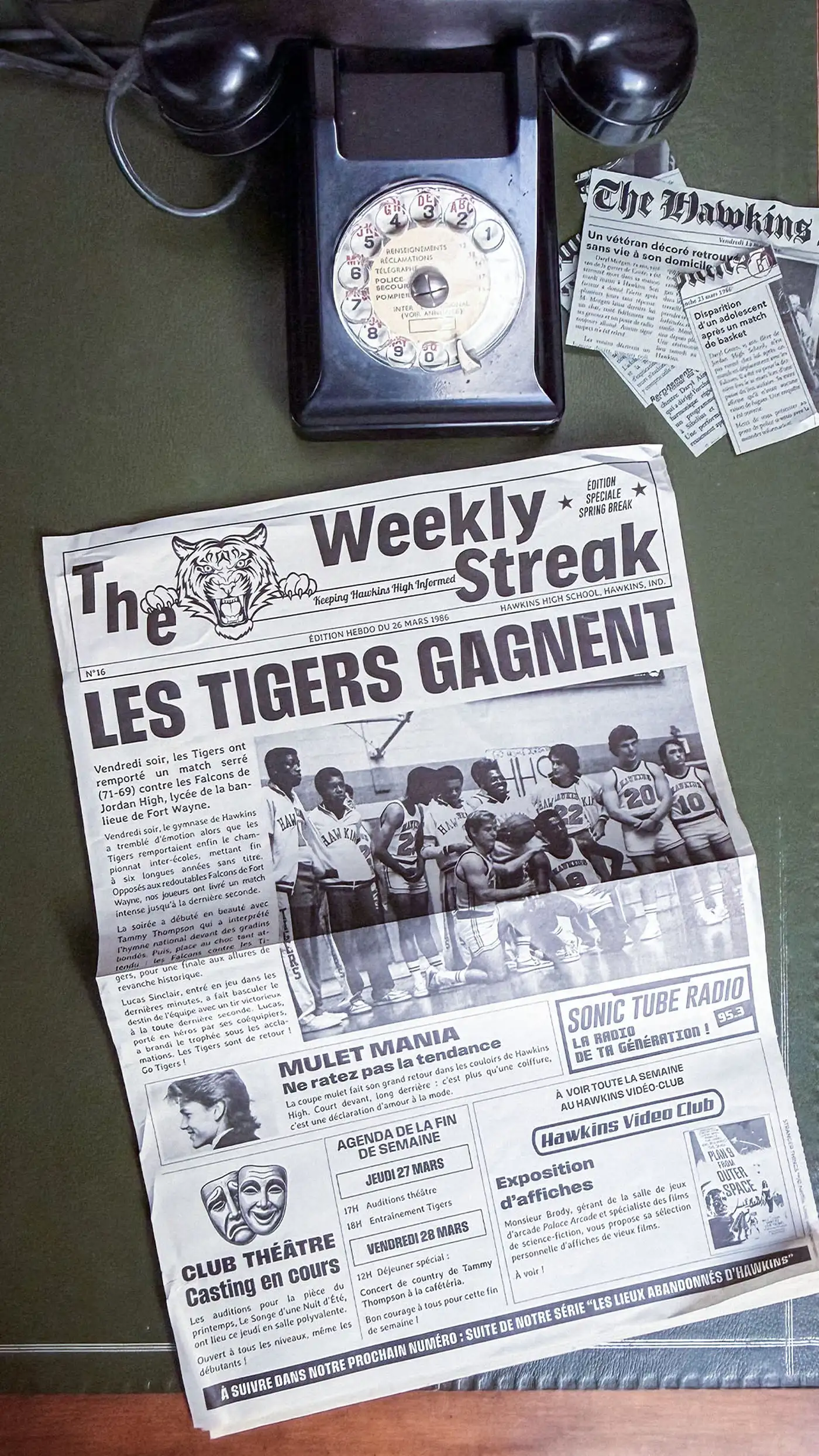 Vintage rotary phone on a green desk beside The Weekly Streak school newspaper and Hawkins Post clippings