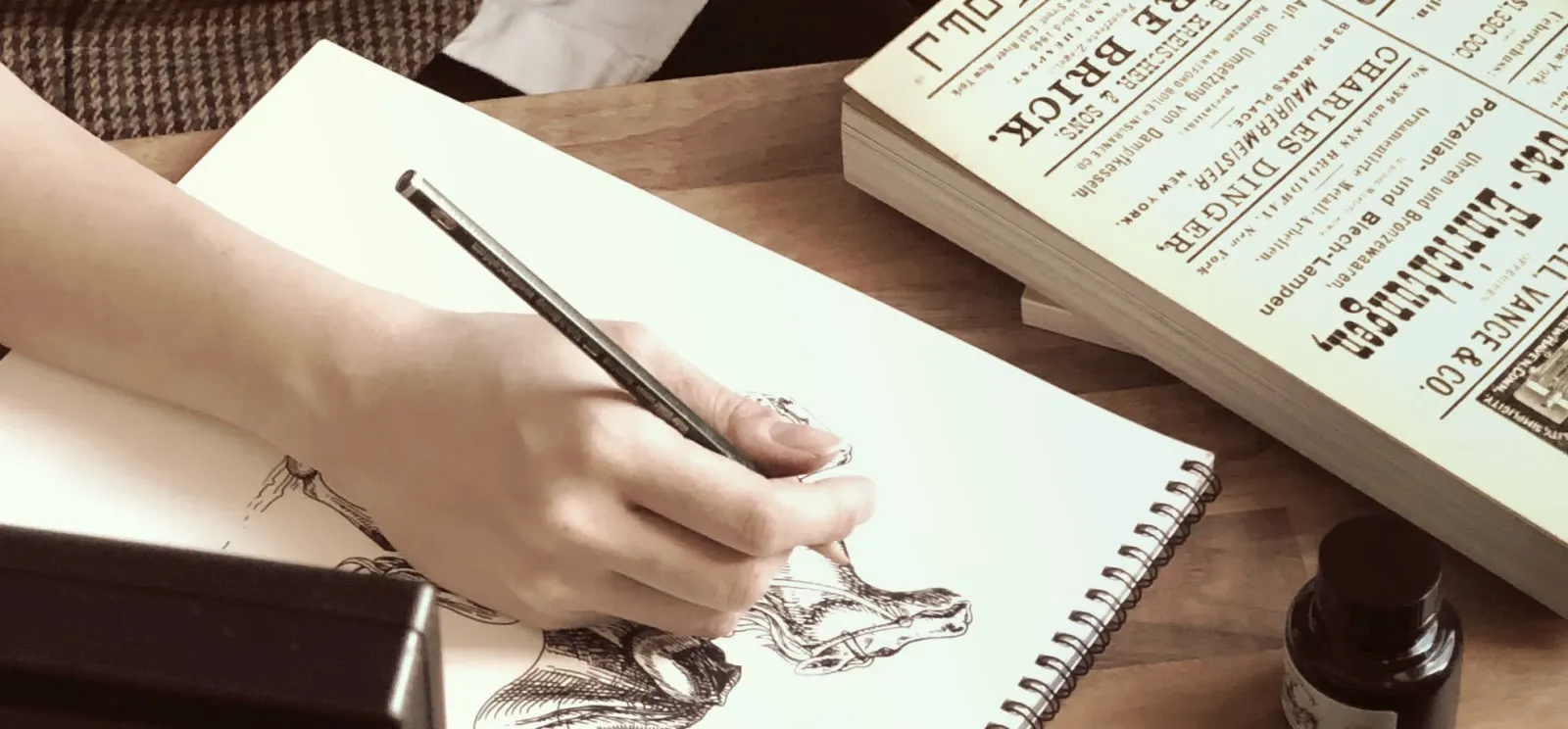 Une main dessine une créature dans un carnet à côté d'un encrier.