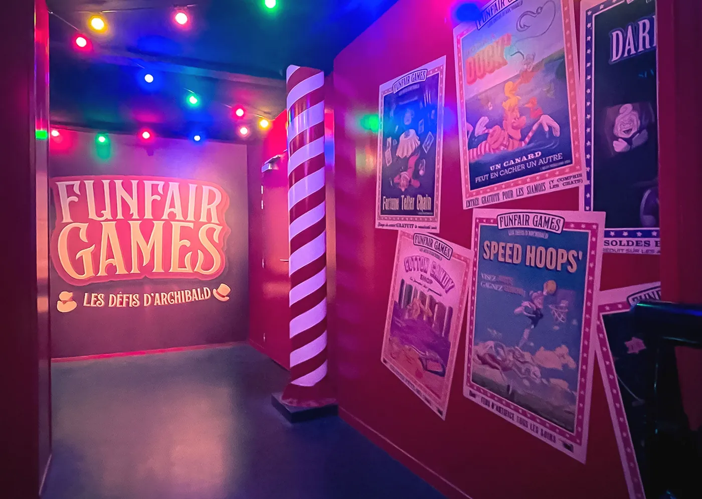 Salle immersive Funfair Games avec des affiches d'attractions vintage sous un éclairage de fête foraine.