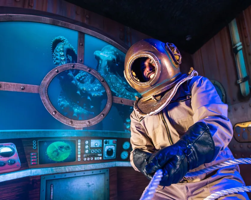 Un plongeur en scaphandre à casque de cuivre aux commandes d'un décor de sous-marin immersif.
